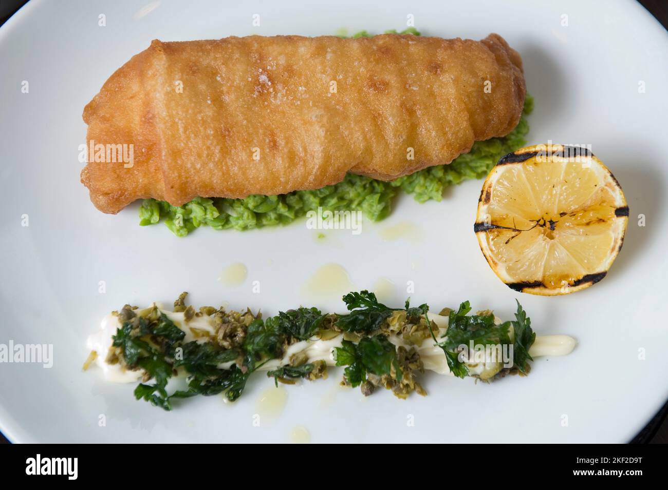 Fisch und Chips auf einer grünen Erbsen-Creme und einem Kaper-Mayonnaise-Salat serviert. Stockfoto