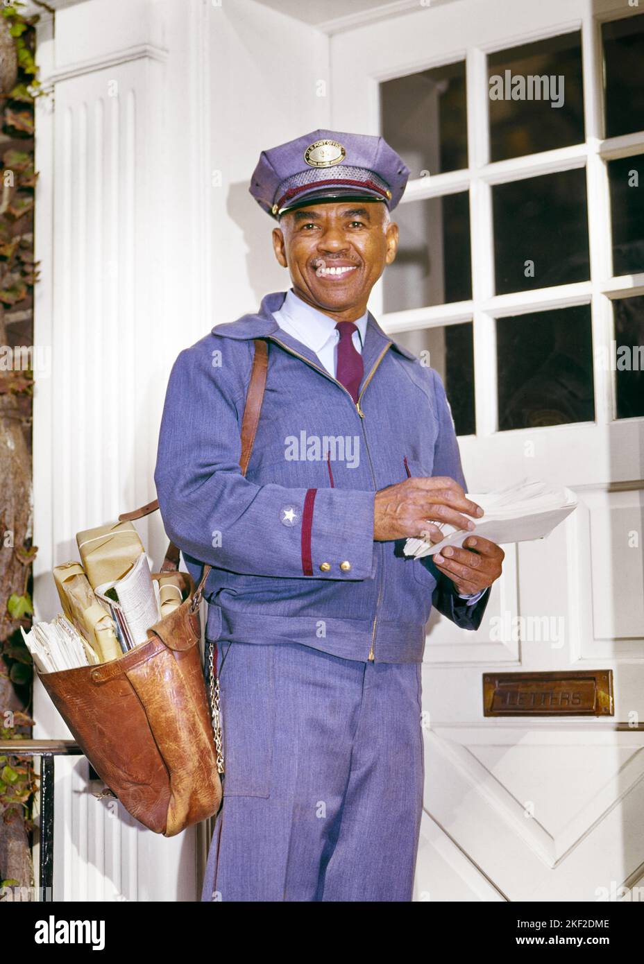 1960S PORTRAIT LÄCHELNDER AFROAMERIKANISCHER POSTBOTE, DER DIE POST VOR DER TÜR STEHEND IN POSTUNIFORM AUF DIE KAMERA SCHAUTE - KP1087 HAR001 HARS KOPIEREN RAUM HALBE LÄNGE PERSONEN POST MÄNNER MITTLEREN ALTERS MANN LIEFERN BLICKKONTAKT GESCHICKLICHKEIT BERUF GLÜCK FÄHIGKEITEN FRÖHLICHEN KUNDENSERVICE AFRO-AMERIKANER AFRO-AMERIKANISCHE SCHWARZE ETHNISCHE ZUGEHÖRIGKEIT ARBEIT STOLZ BESCHÄFTIGUNG BERUFE LÄCHELT POSTSENDUNG FREUDIGE POSTTASCHE VOR DER TÜR MITARBEITER USPS BEAMTER VEREINT STATES POSTAL SERVICE HAR001 ARBEITEN ALTMODISCHE AFROAMERIKANER Stockfoto