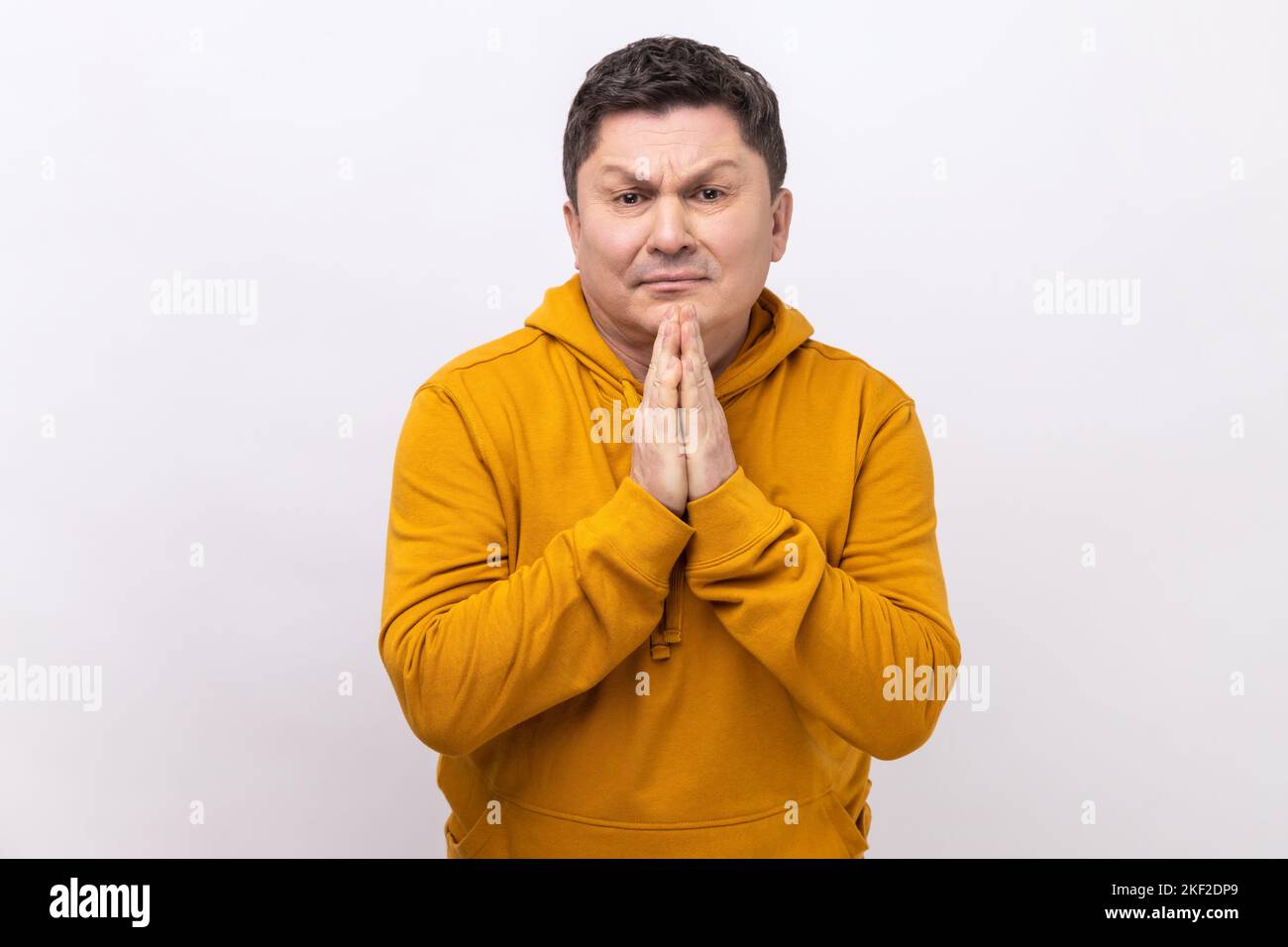 Bitte, ich bette. Portrait eines verärgerten Brünetten Mannes, der die Arme im Gebet hält, Hilfe oder Vergebung mit anflehenden Augen bittet und einen Kapuzenpullover im urbanen Stil trägt. Innenaufnahme des Studios isoliert auf weißem Hintergrund. Stockfoto