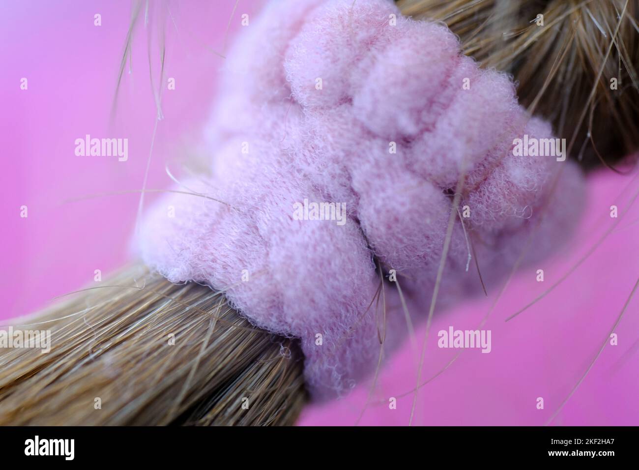 Makrobild eines Haarbandes im Kinderhaar. Nahaufnahme eines rosafarbenen Materials mit rosafarbenem Hintergrund. Gesundheit und Schönheit. Stockfoto