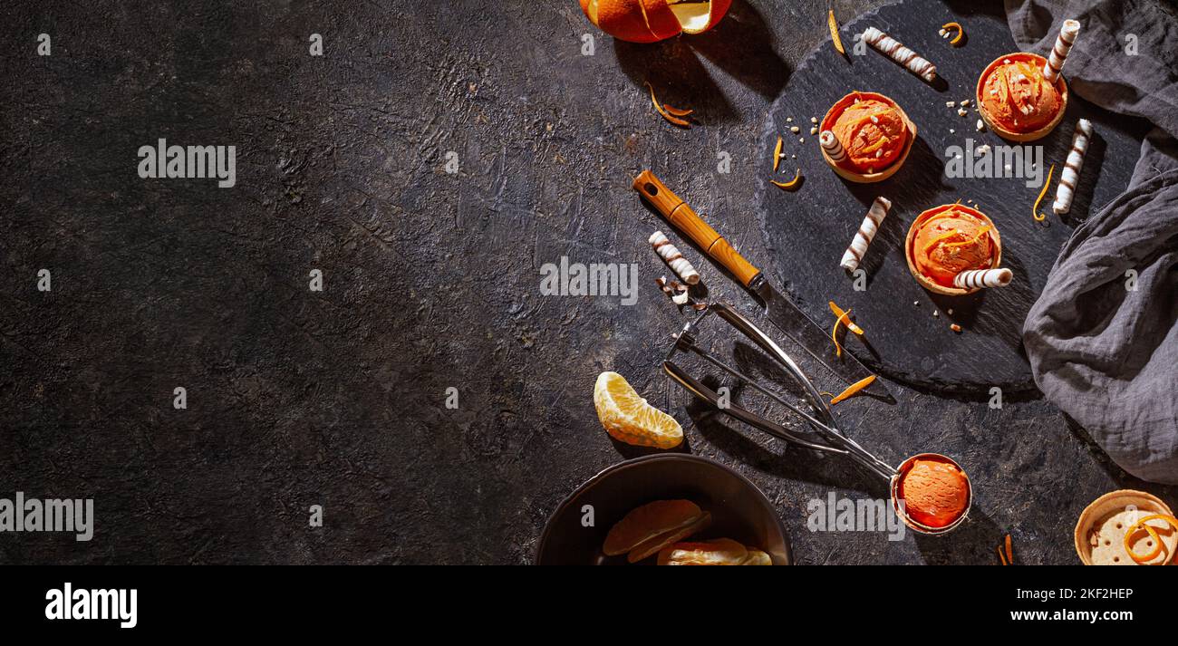 Hausgemachtes Orangeneis auf dunklem Hintergrund mit Eislöffel aus Edelstahl, horizontales Banner mit Platz für Text, flach liegend Stockfoto