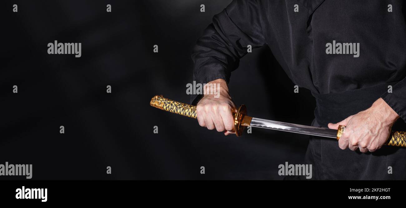 Der Samurai hält ein japanisches Katana-Schwert, Banner. Foto eines Kriegers in schwarzer Kleidung in niedriger Tonart mit Platz für Text Stockfoto