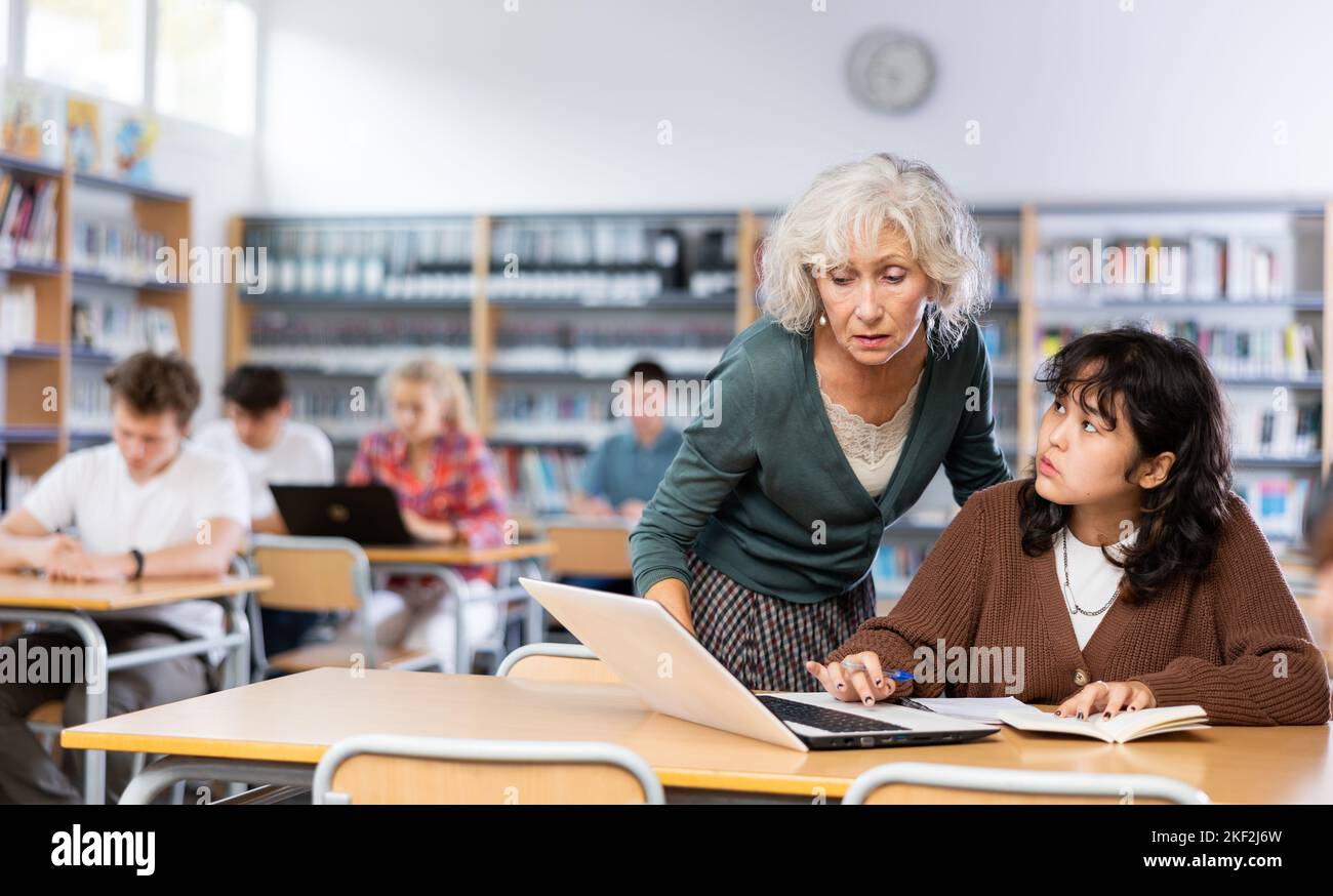 Ältere Lehrerin hilft Schülerinnen, die Gleichung in der Schulbibliothek zu lösen Stockfoto