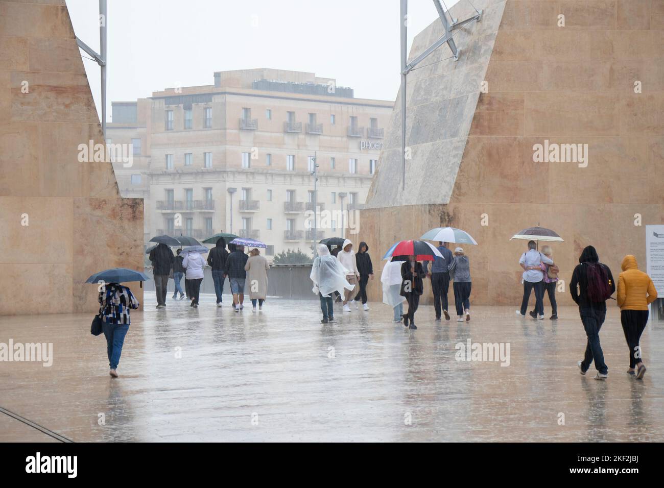 Valletta, Malta - 12. November 2022: Menschen, die Regenponchos tragen und Regenschirme halten, laufen an einem regnerischen Tag Stockfoto