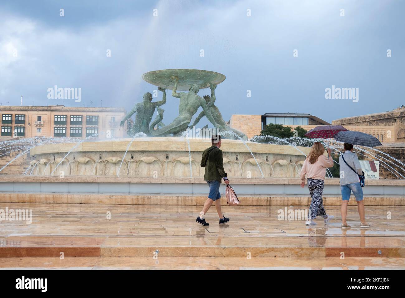 Valletta, Malta - 12. November 2022: Menschen, die an einem regnerischen Tag unter Sonnenschirmen am Triton-Brunnen spazieren Stockfoto