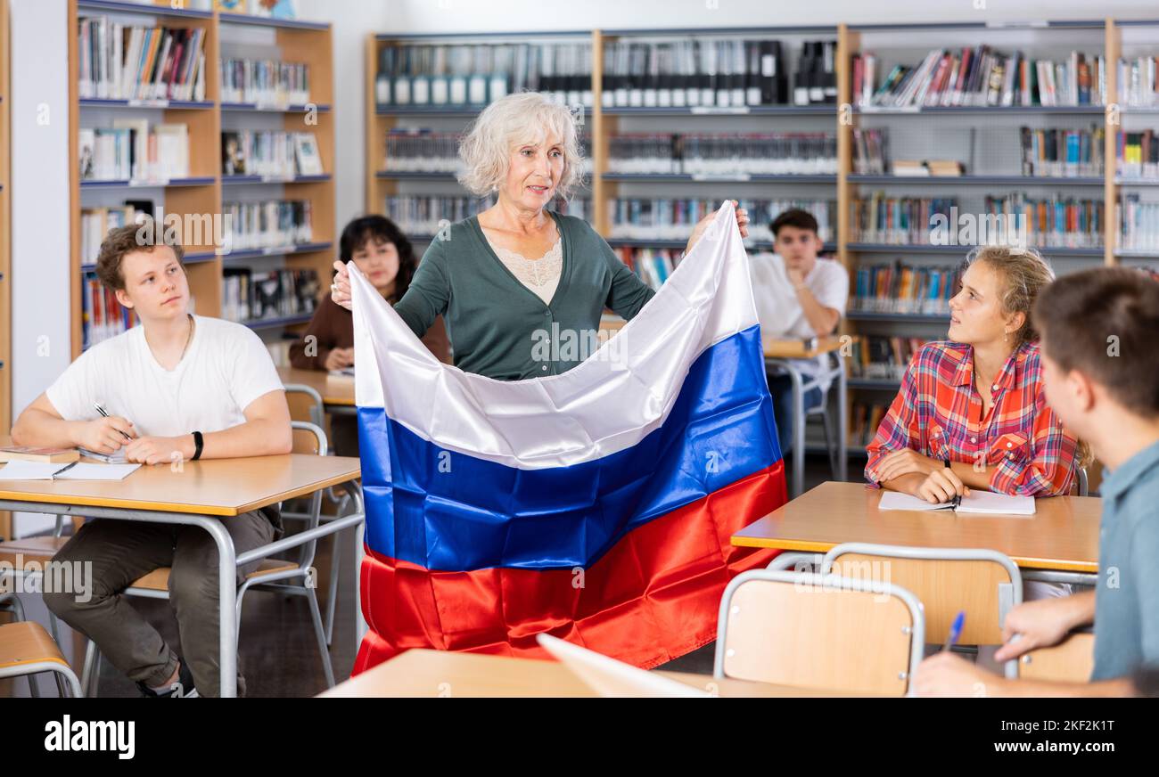 Interessante Geschichte über Russland während der Unterrichtung von Schülern in der Schulbibliothek. Die Lehrerin hält die russische Flagge in ihren Händen Stockfoto