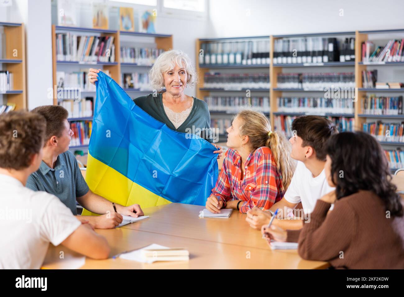 Interessante Geschichte über die Ukraine während der Unterrichtung von Schülern in der Schulbibliothek. Die Lehrerin hält die Flagge der Ukraine in ihren Händen Stockfoto