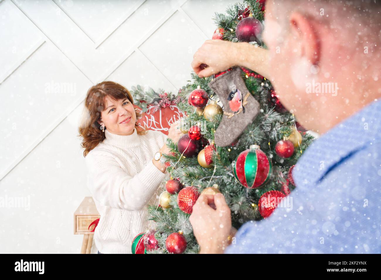 Lächelndes, glückliches Paar im mittleren Alter, das Weihnachtsbaum zu Hause schmückt. Glückliches Paar zusammen zu Hause, weihnachtskonzept Stockfoto