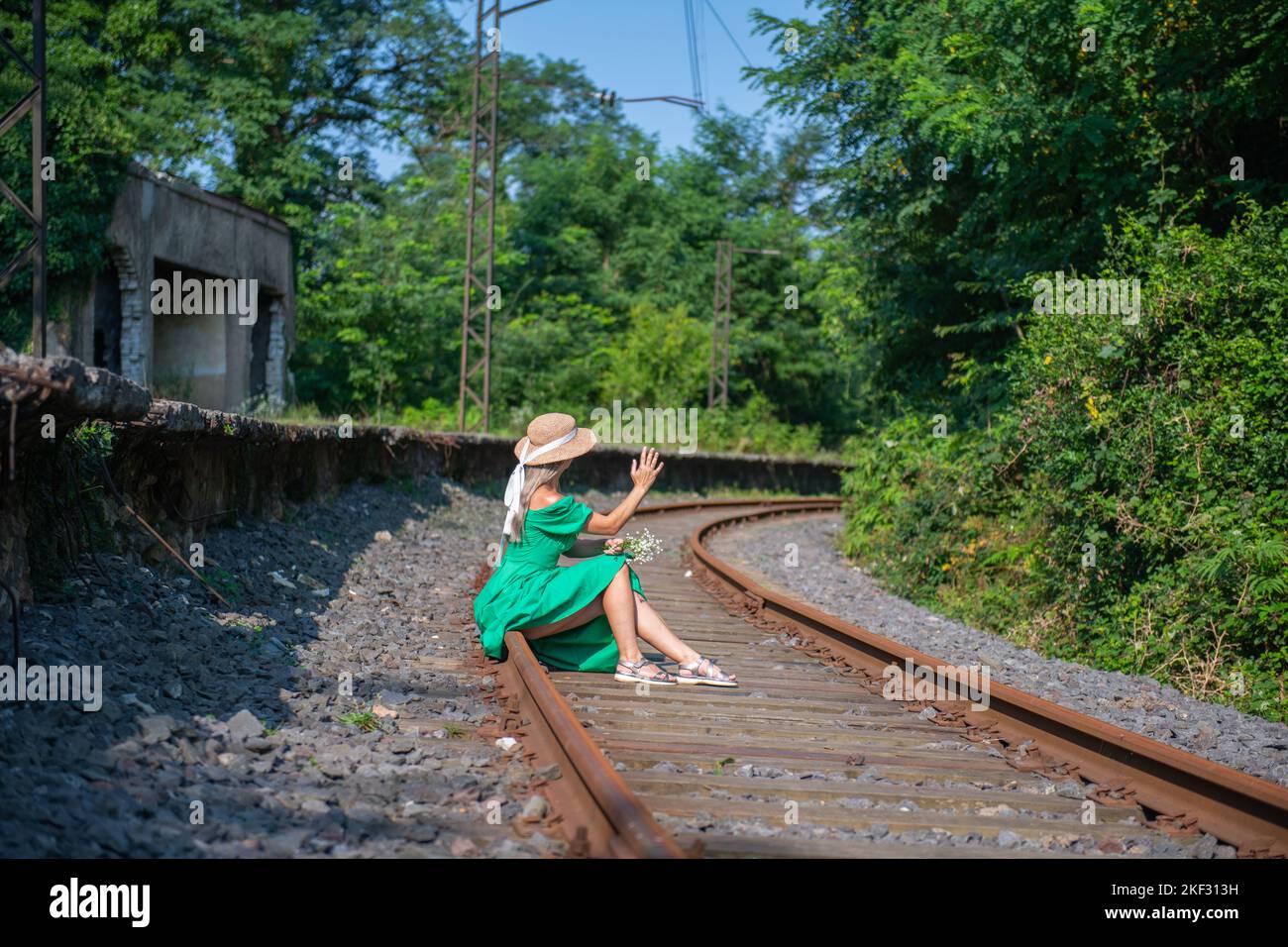 Eine junge Frau in einem grünen Kleid sitzt auf der Eisenbahn Stockfoto