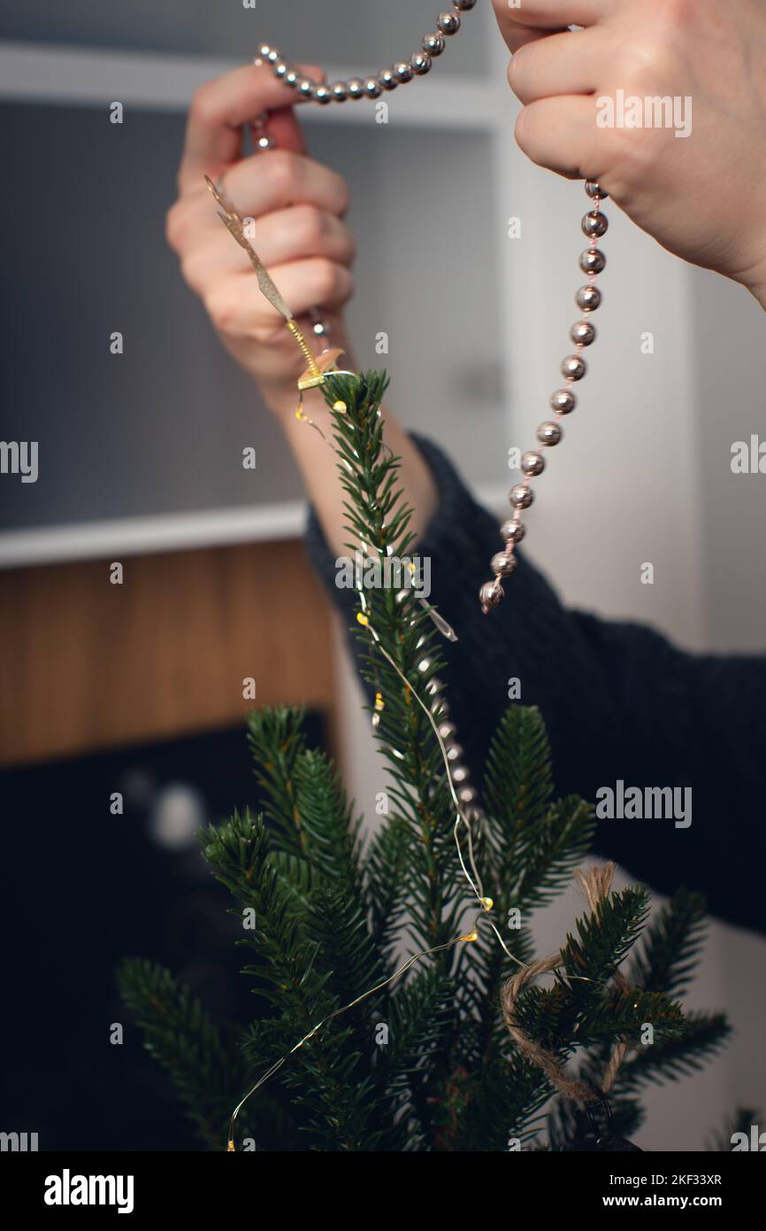 Ein Mädchen schmückt einen Weihnachtsbaum zu Weihnachten mit Bällen. Vorderansicht. Vertikales Foto. Stockfoto