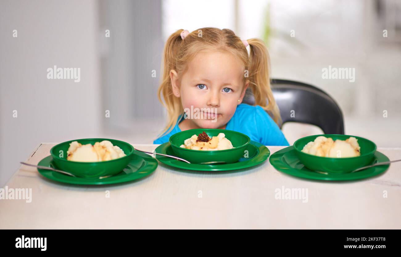 Kein Kind sollte hungrig sein. Porträt eines kleinen Mädchens, das an einem Esstisch sitzt und von Freiwilligen Essen zur Verfügung gestellt wird. Stockfoto