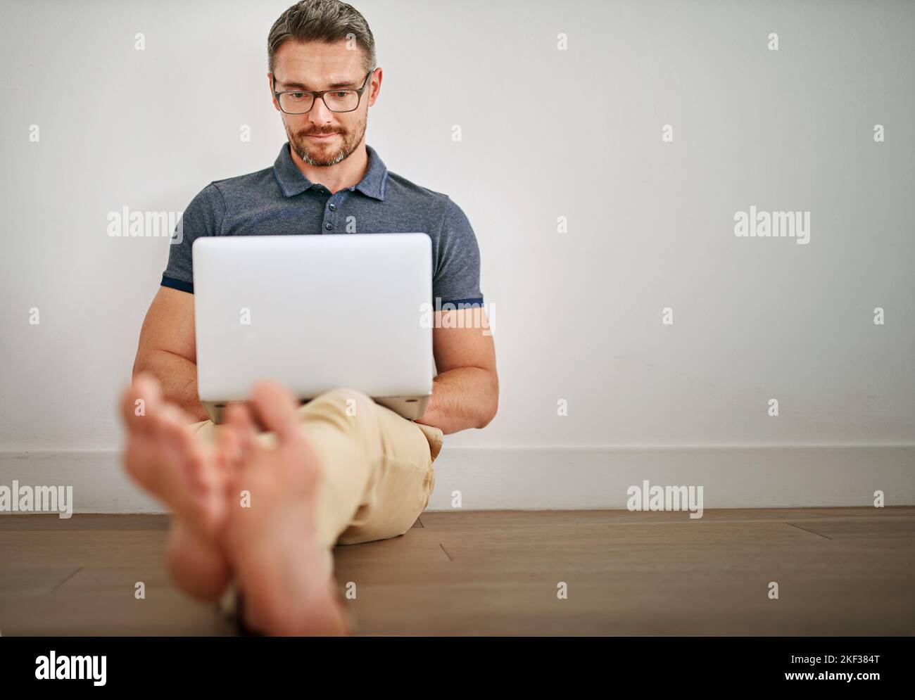 Ein Mann, der seinen Laptop benutzt, während er an einer Wand sitzt. Stockfoto