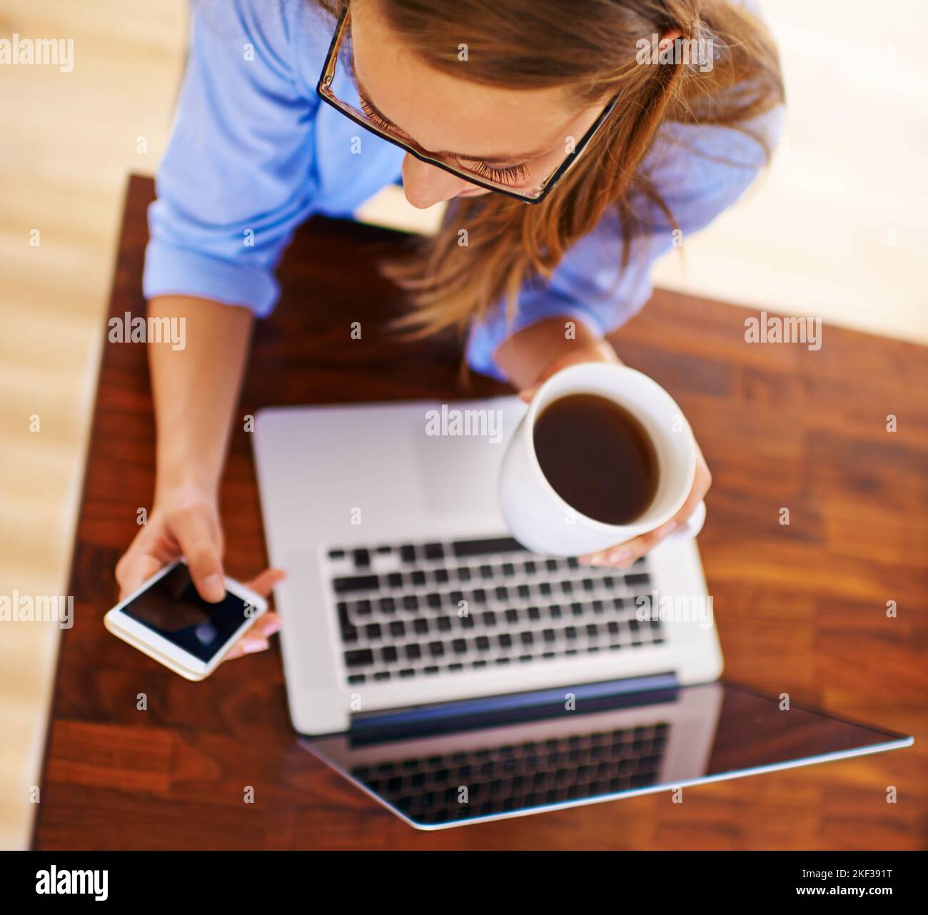 Kurztext wird gesendet. High-Angle-Aufnahme einer jungen Frau, die mit ihrem Laptop und Mobiltelefon Kaffee getrunken hat. Stockfoto