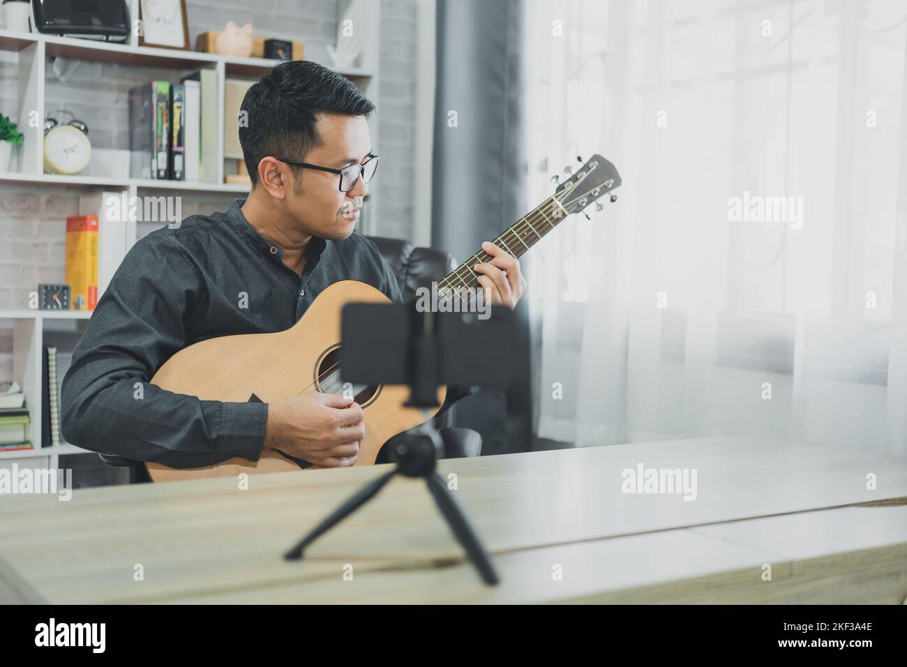 Asiatischer Musiklehrer Mann sendet live Gitarrenunterricht an Schüler online mit Handy. Asiatischer männlicher Musiker spielt Gitarre und singt live Video confer Stockfoto