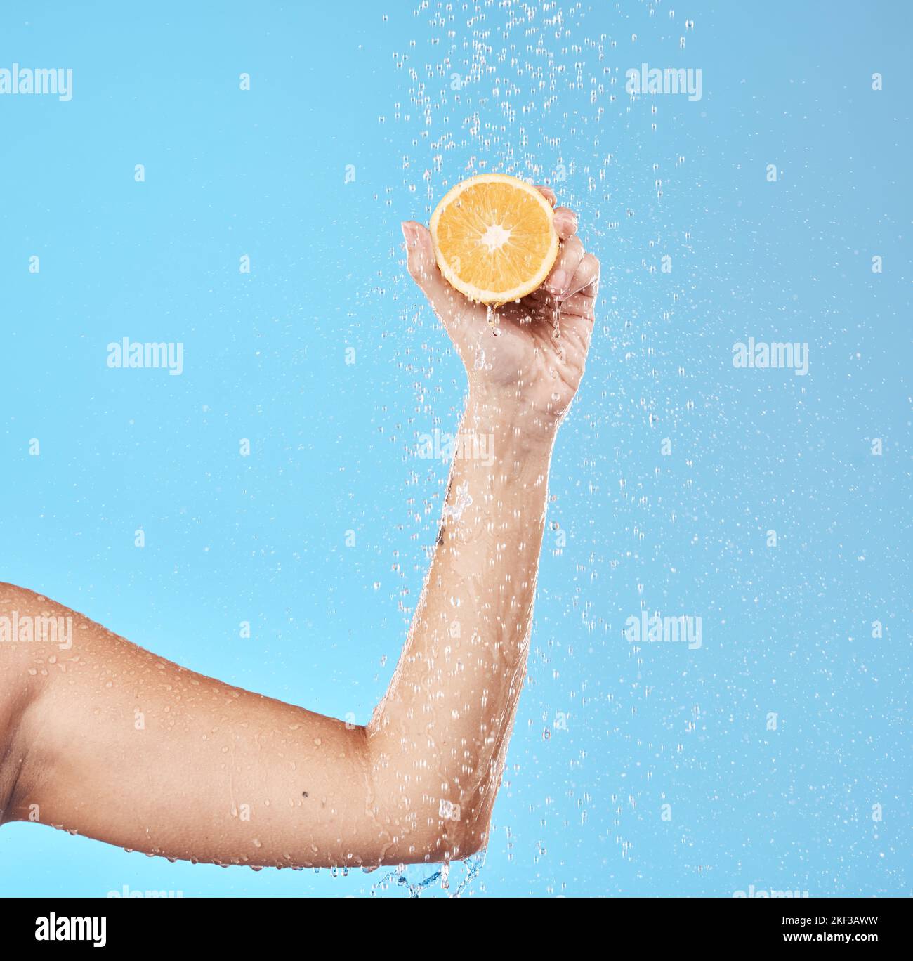 Hand, Orange und Wasser mit einer Frau im Studio auf blauem Hintergrund für Gesundheit oder Flüssigkeitszufuhr. Essen, Luxus und Wellness mit einer Frau, die Früchte trägt Stockfoto