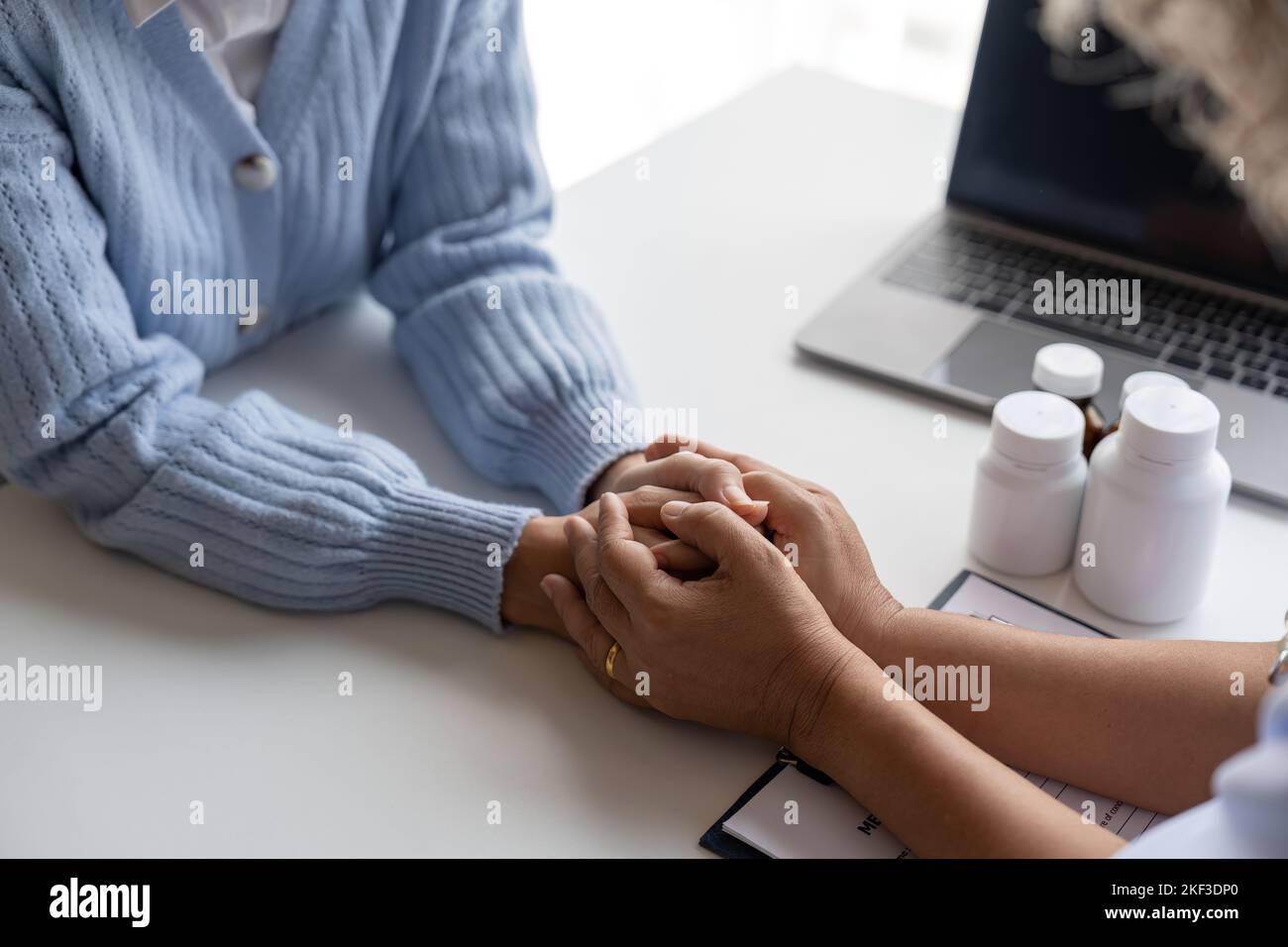 Doktor gibt Hoffnung. Nahaufnahme einer jungen Ärztin, die sich nach vorne lehnt, um eine lächelnde ältere Patientin zu sehen, die ihre Hand in Handflächen hält. Hausmeisterin Stockfoto