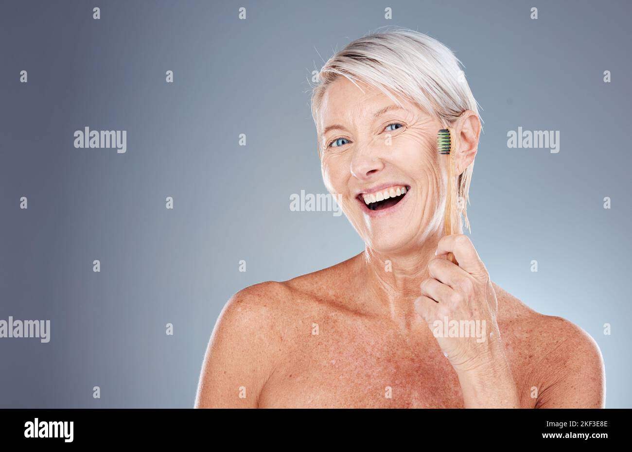 Zahn-, Wellness- und Porträt der alten Frau mit Zahnbürste in der Hand auf grauem Hintergrund Studio. Umweltfreundlich, Mundhygiene und ältere Weibchen mit Bambus Stockfoto