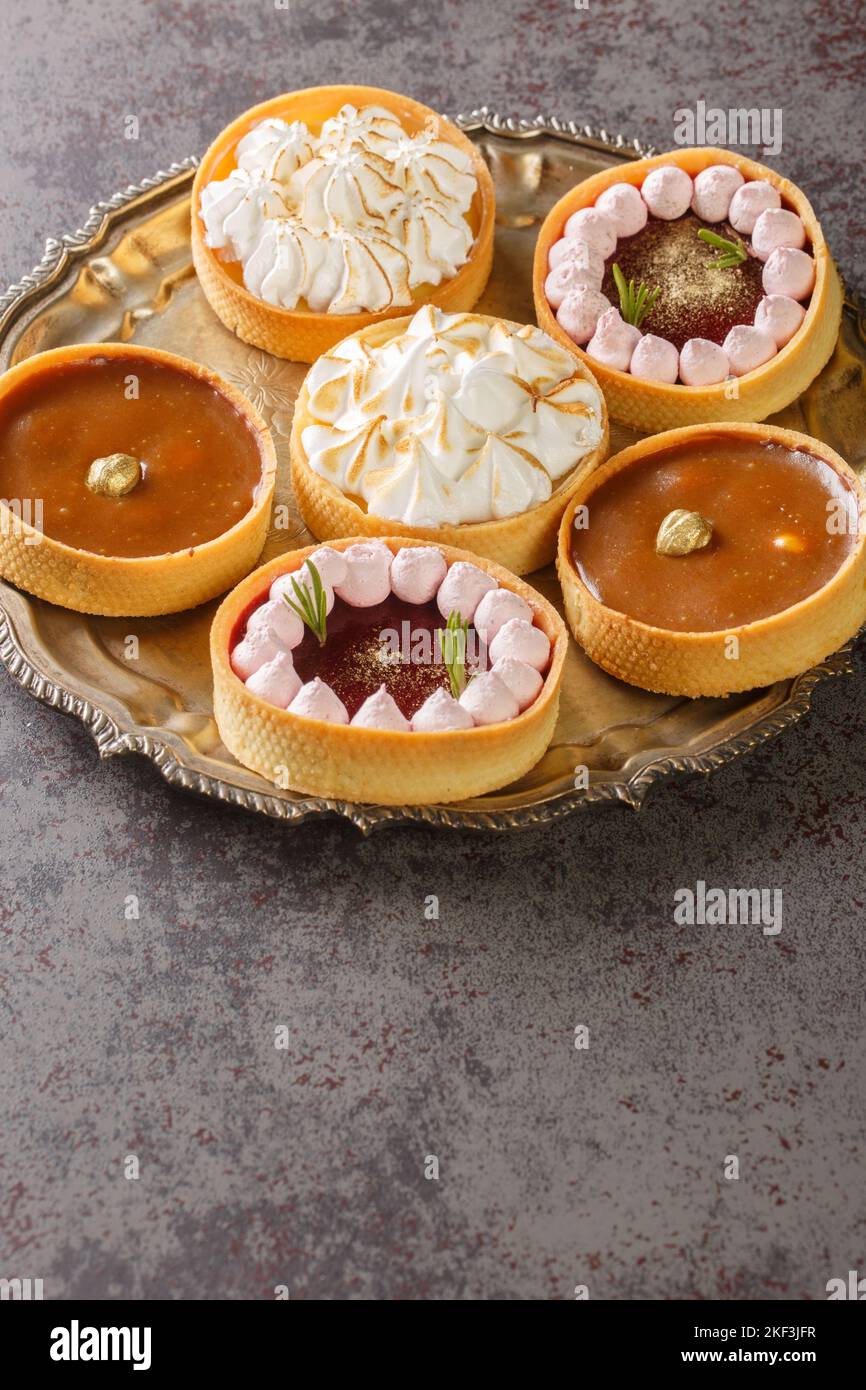 Schöne Törtchen mit Baiser und Zitronenquark, Himbeer-Mousse, Nüssen und Schokolade aus nächster Nähe auf einem Teller auf dem Tisch. Horizontal Stockfoto