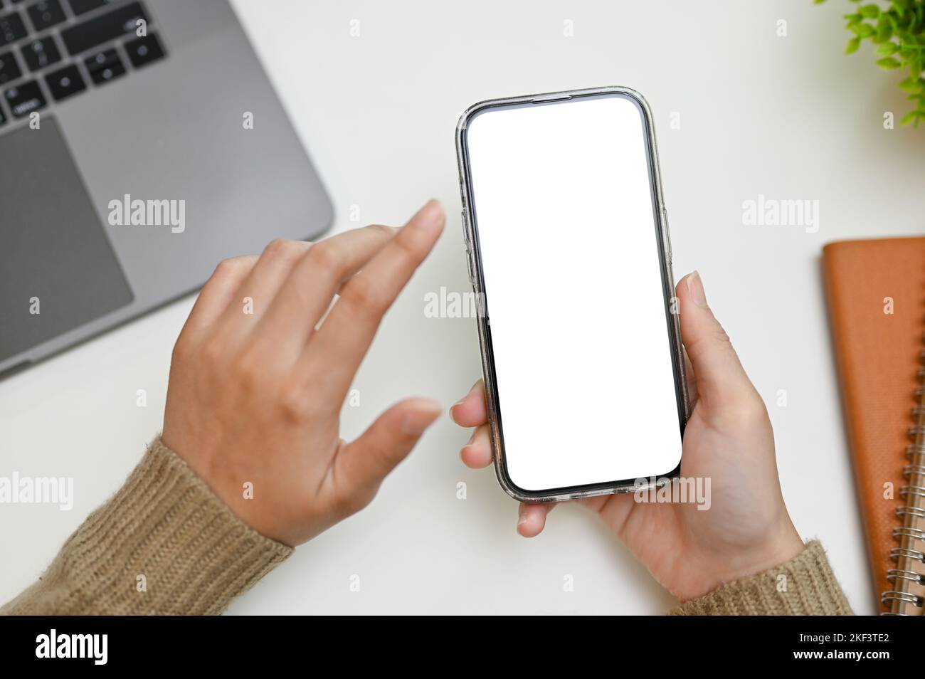 Eine Frau, die ihr Smartphone über ihrem Schreibtisch benutzt. Telefon-White-Screen-Mockup zur Anzeige Ihres grafischen Banners. Stockfoto