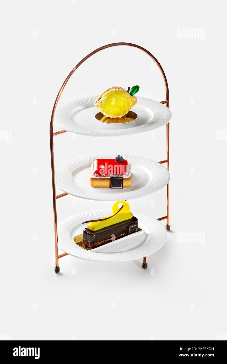Dreistufiger Dessertständer mit zitronenförmigem Kuchen, kleinem Käsekuchen mit Beerengelee und Schokoladenkuchen mit Bananenmousse Stockfoto