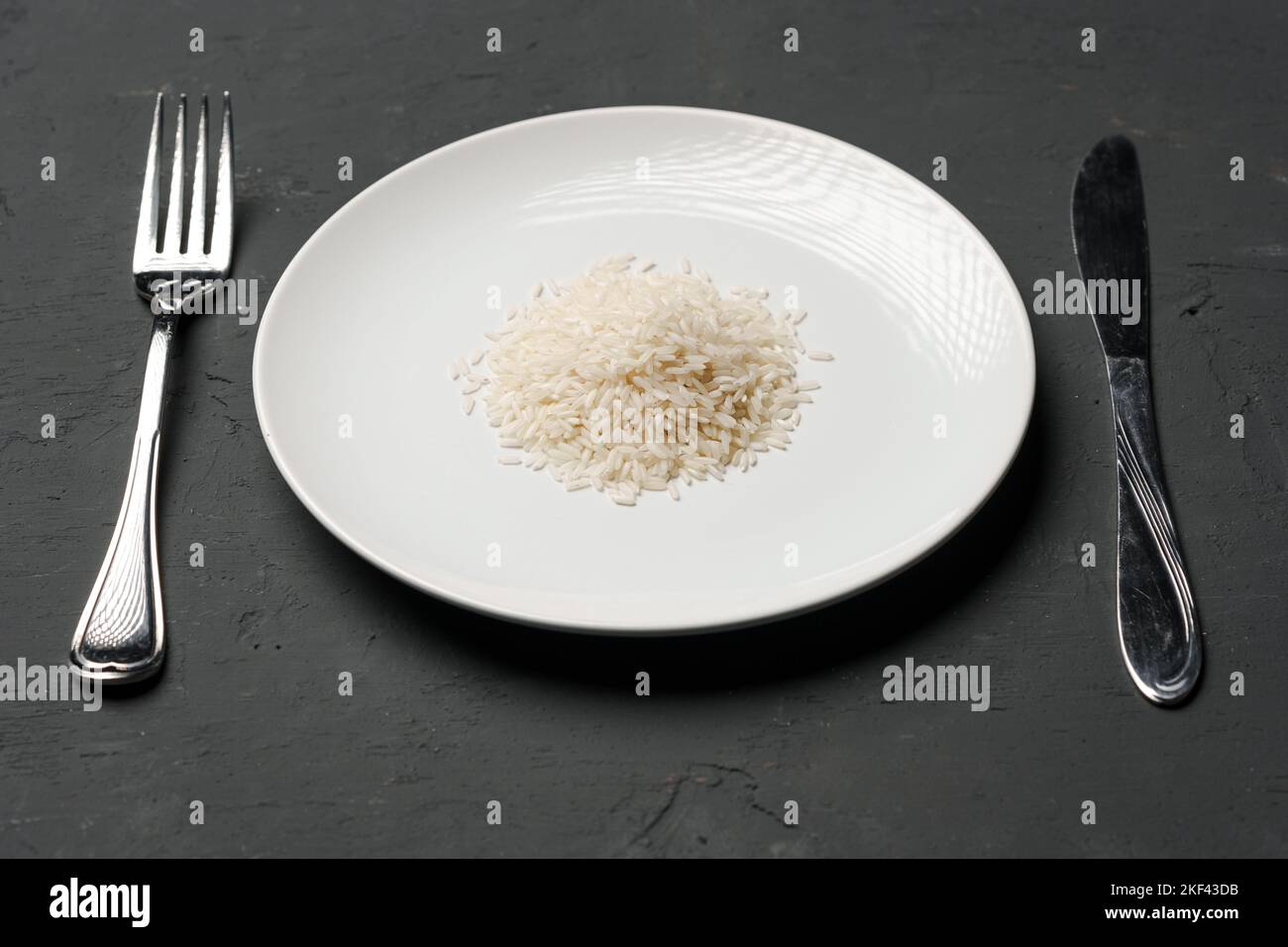 Haufen von trockenem Reis in einer Schüssel auf schwarzem Hintergrund, Mangel an Nahrung, Hunger-Konzept Stockfoto