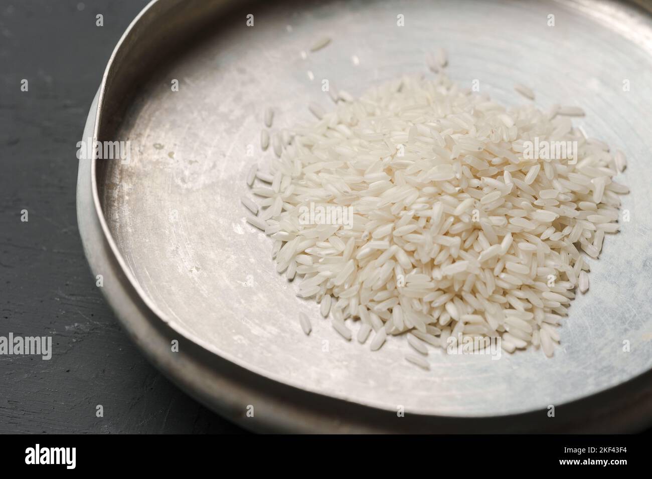 Haufen von trockenem Reis in einer Schüssel auf schwarzem Hintergrund, Mangel an Nahrung, Hunger-Konzept Stockfoto