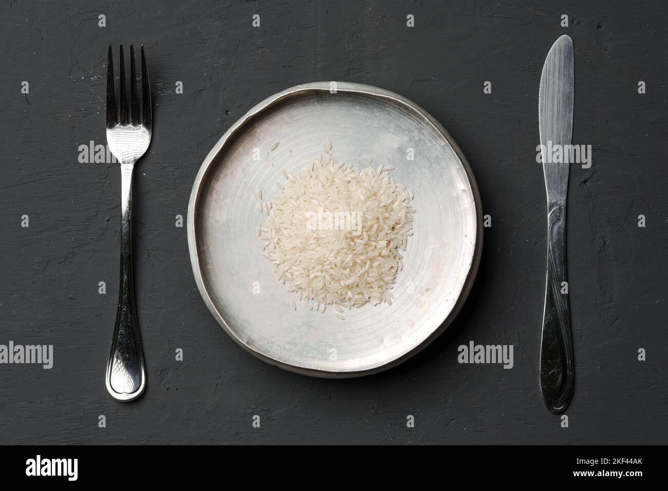 Haufen von trockenem Reis in einer Schüssel auf schwarzem Hintergrund, Mangel an Nahrung, Hunger-Konzept Stockfoto