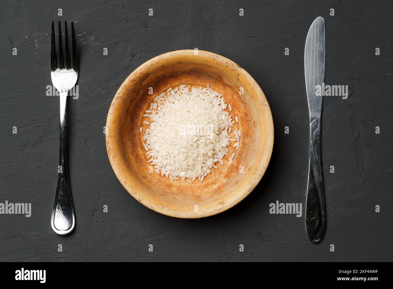 Haufen von trockenem Reis in einer Schüssel auf schwarzem Hintergrund, Mangel an Nahrung, Hunger-Konzept Stockfoto