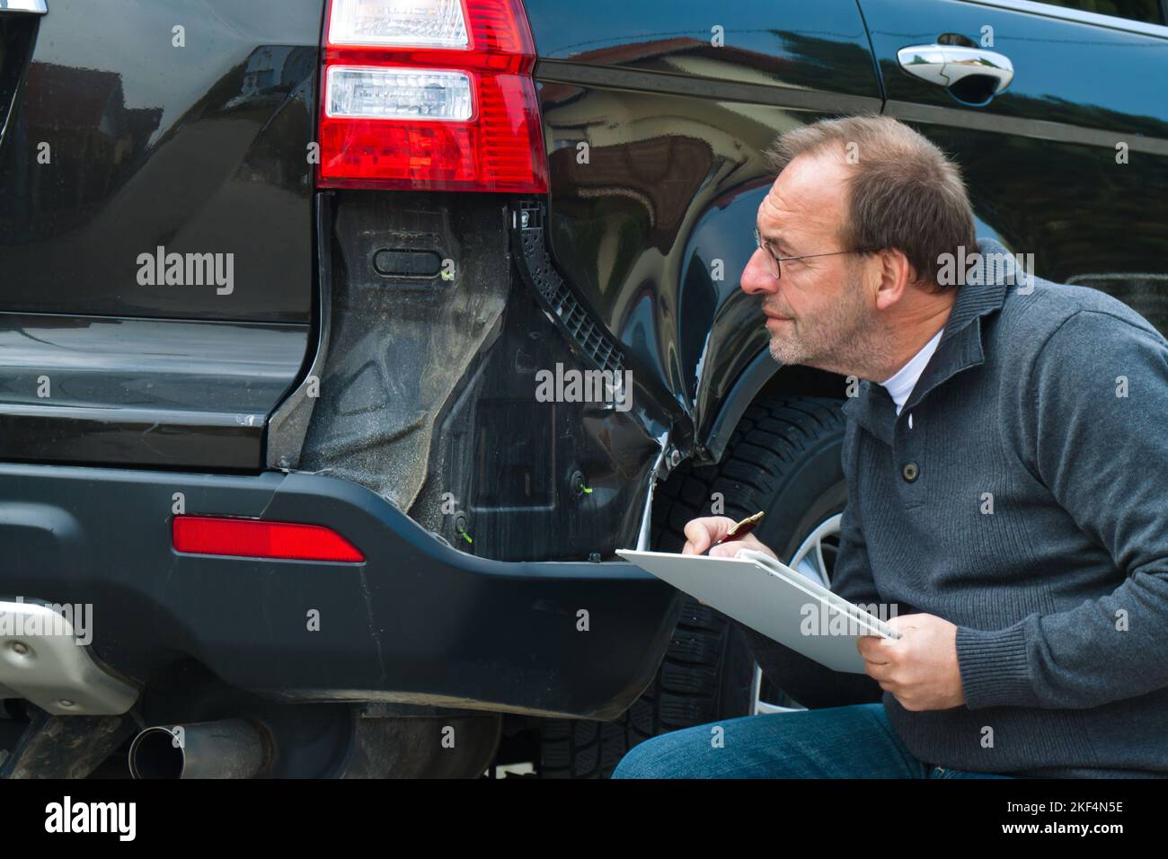 KFZSachverarbeiter einer Versicherung begrueft einen Schaden am Auto. Autoversicherung