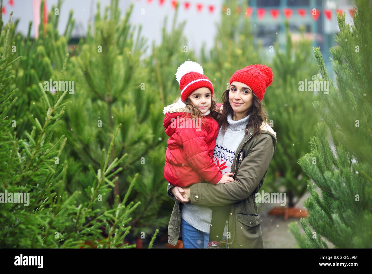 Mutter hält ihre Tochter vor dem Hintergrund vieler Weihnachtsbäume und Schnee in den Armen. Stockfoto
