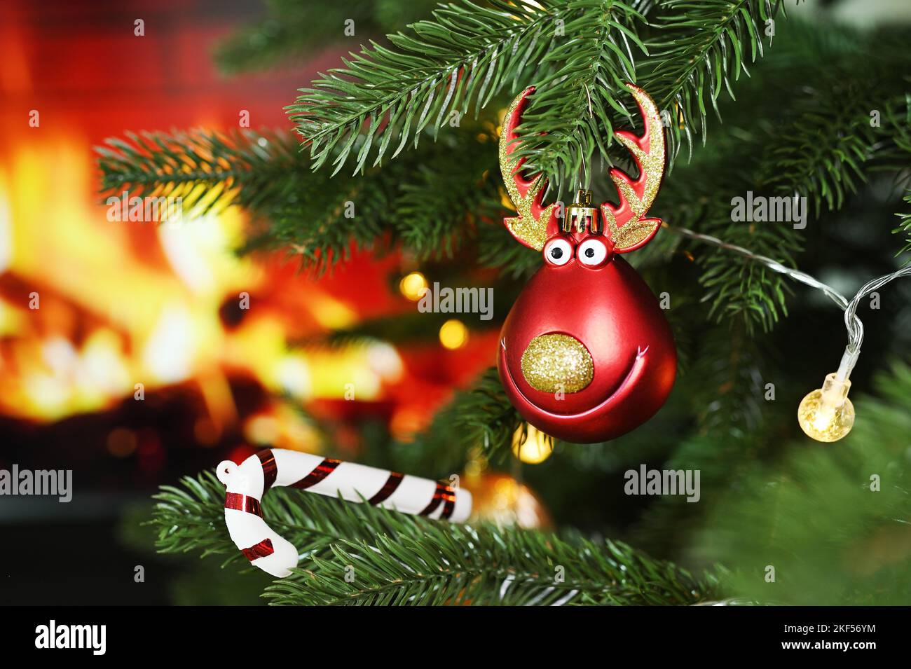 Spielzeug in Form eines roten Hirschkopfes vor dem Hintergrund eines Weihnachtsbaums und eines Kamins. Weihnachtliche Einrichtung Stockfoto