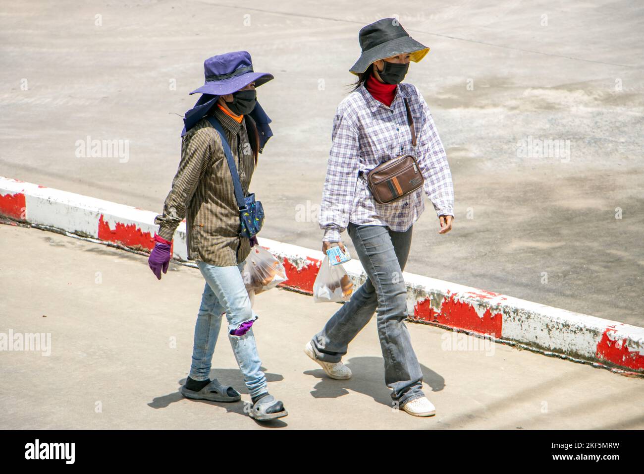 SAMUT PRAKAN, THAILAND, Okt 04 2022, zwei Bauarbeiterinnen mit versteckten Gesichtern gehen eine sonnige Straße entlang Stockfoto