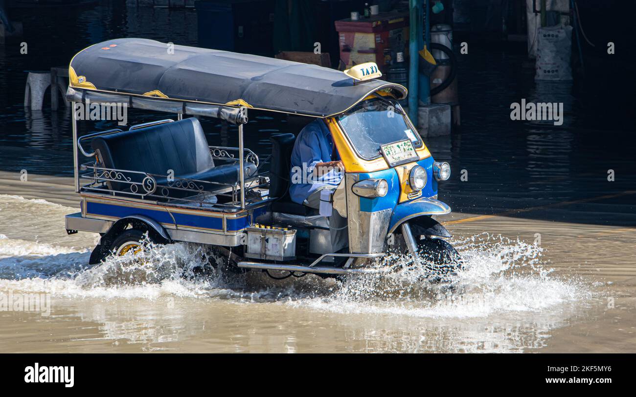 Ein traditionelles motorisiertes Dreirad - Tuk Tuk fährt durch eine überflutete Straße, Thailand Stockfoto