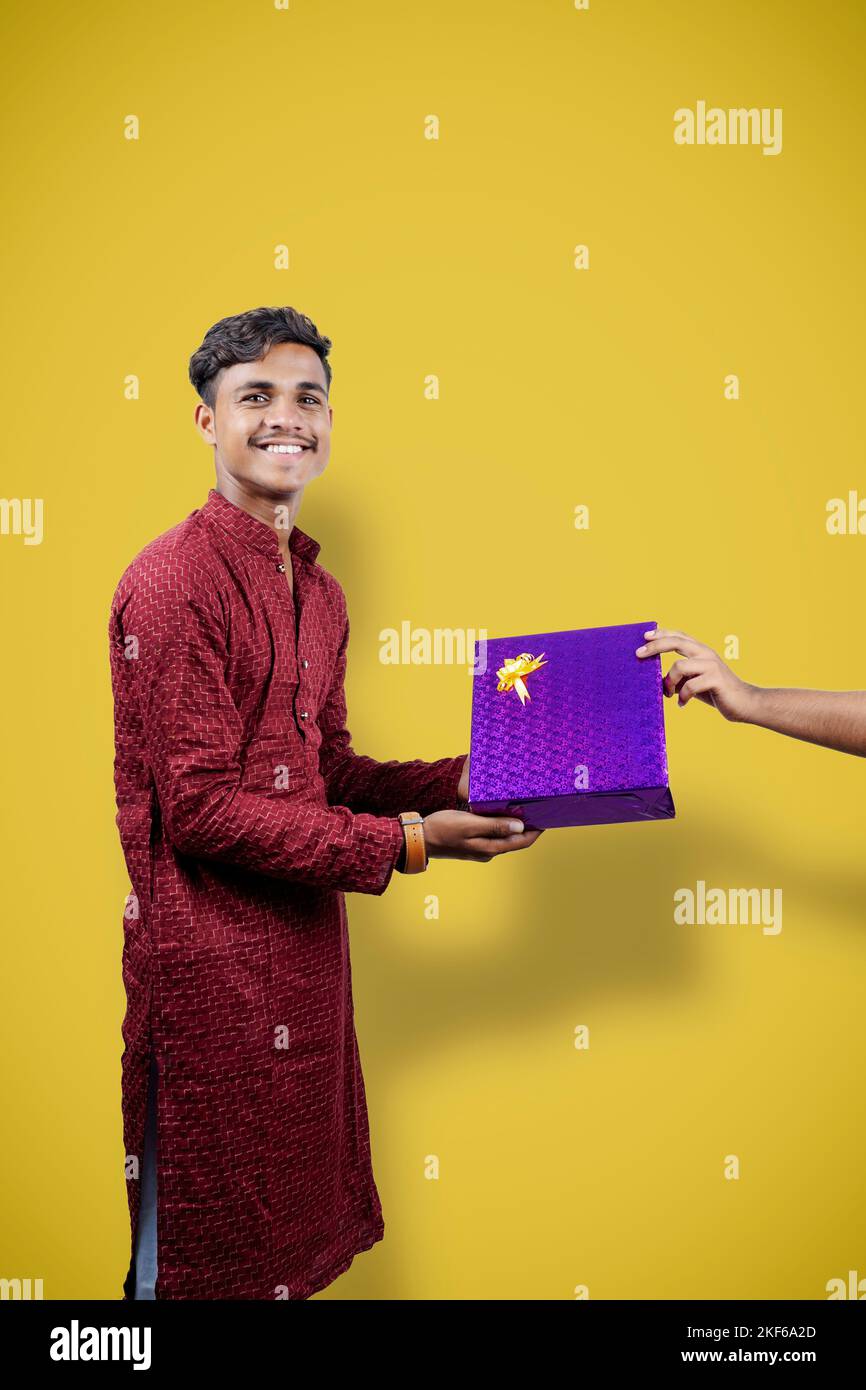 Indischer Mann in ethnischen tragen und erhalten Geschenk-Box von Lieferung Junge , isoliert auf gelbem Hintergrund Stockfoto