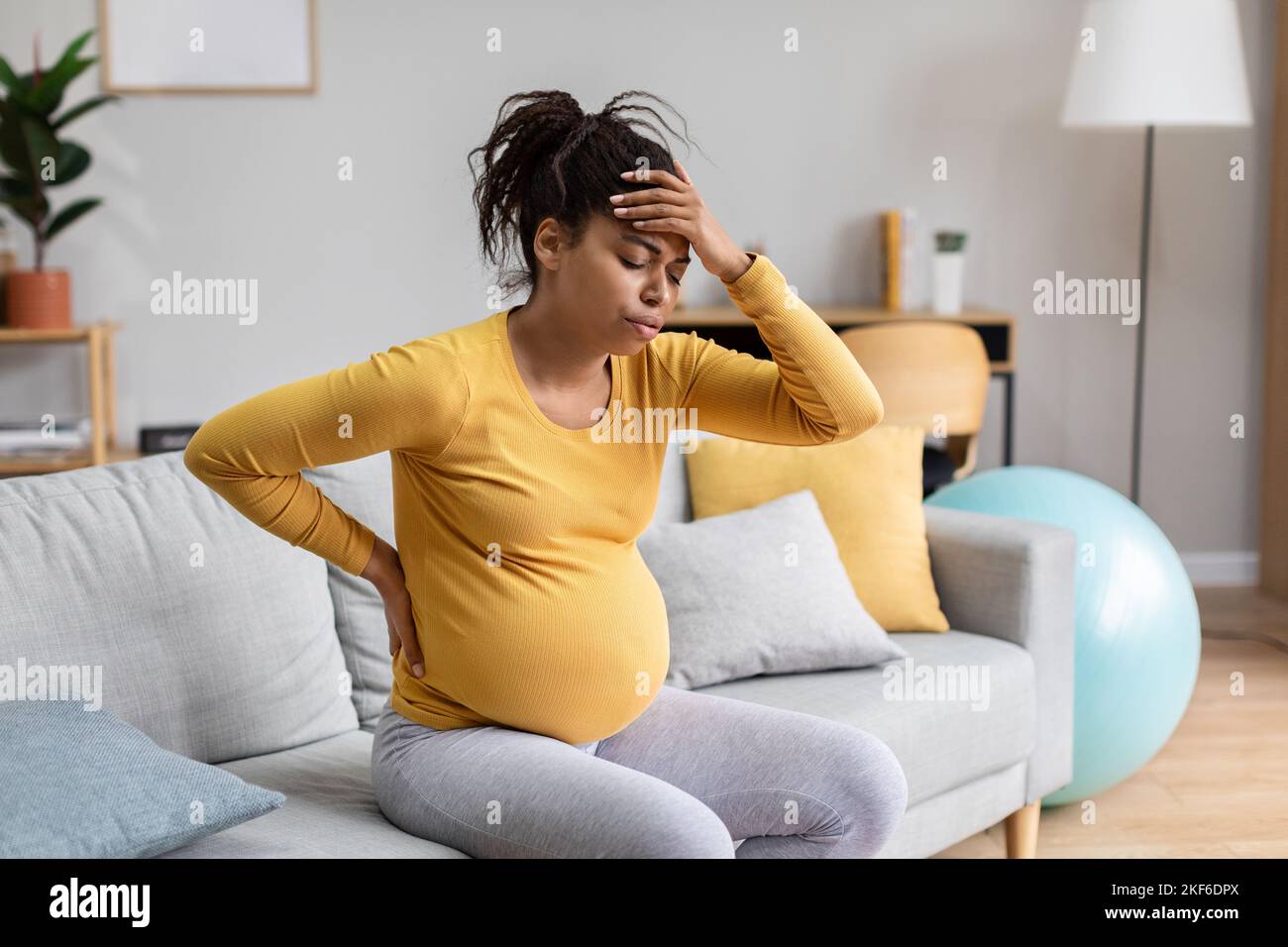 Traurige, unglückliche, junge, schwarze, schwanger Frau, zukünftige Mutter, mit großem Bauch drückt Hand in Kopf und Rücken, leidet unter Schmerzen Stockfoto