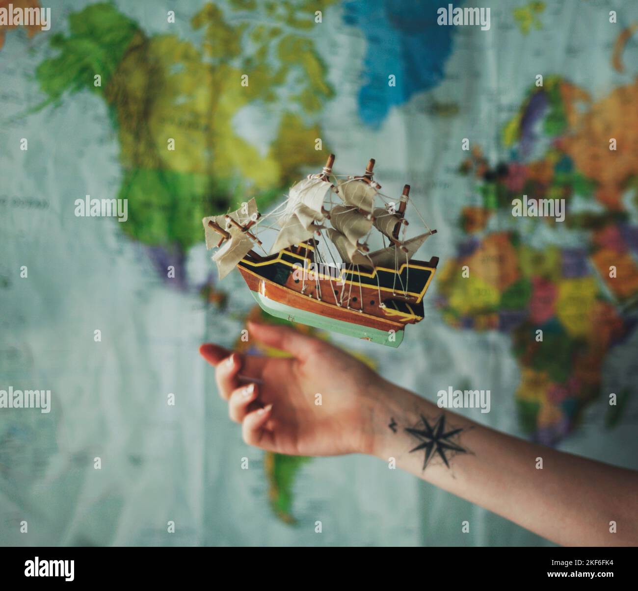 Ein Modellschiff, das vor der Weltkarte schwebt, mit einem Arm mit einem Kompass-Tattoo, das darauf gerichtet ist Stockfoto