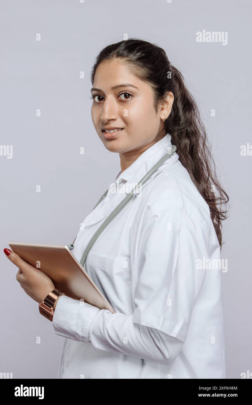 Ein Porträt einer südasiatischen Ärztin, die eine Tablette auf einem grauen Hintergrund hält Stockfoto