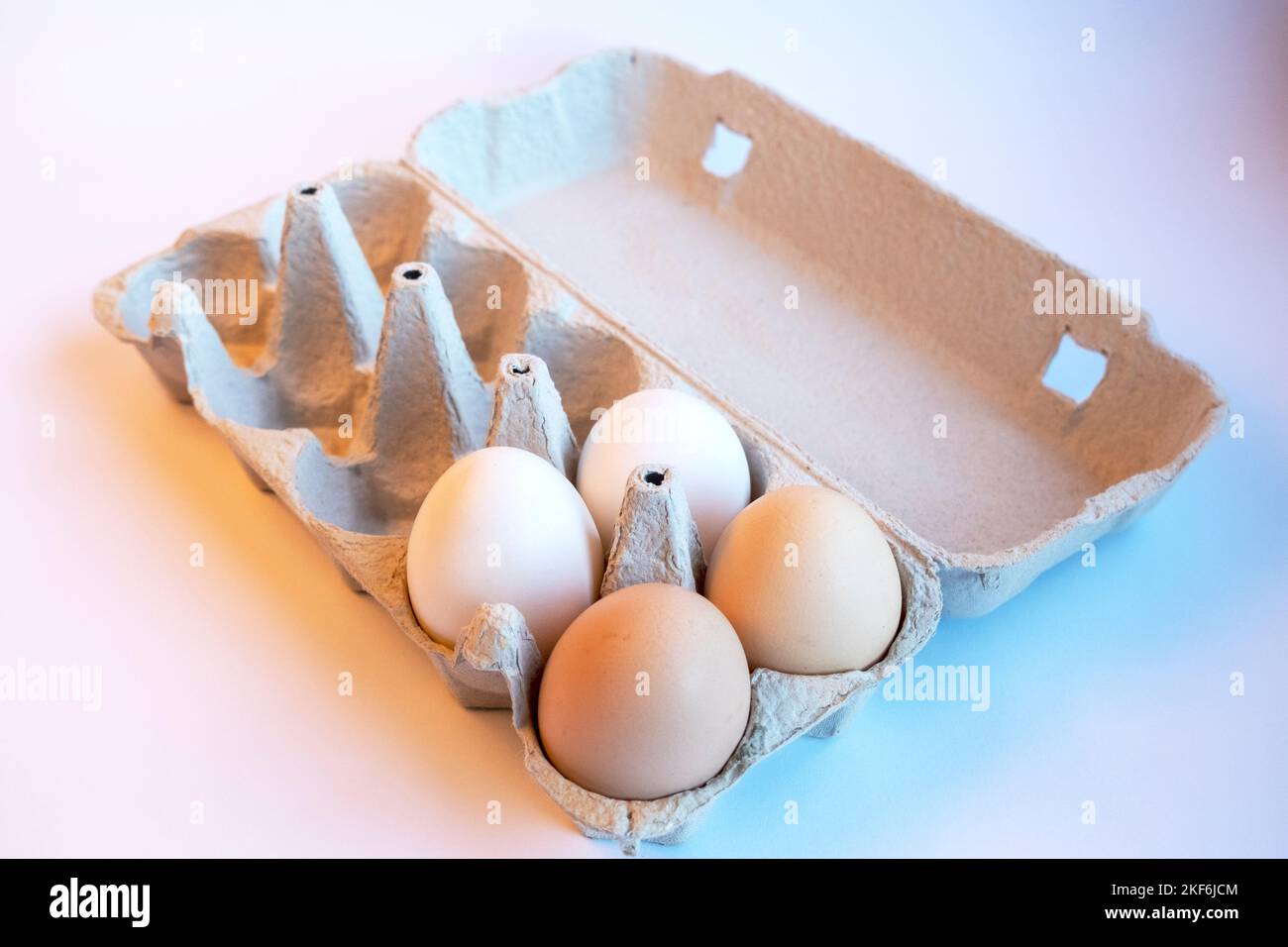 Frische zwei hellbraune und zwei weiße Eier in einer Papierbox und sechs leere Plätze für gesunde Lebensmittel. Eierbehälter aus recycelbarem Material. Stockfoto