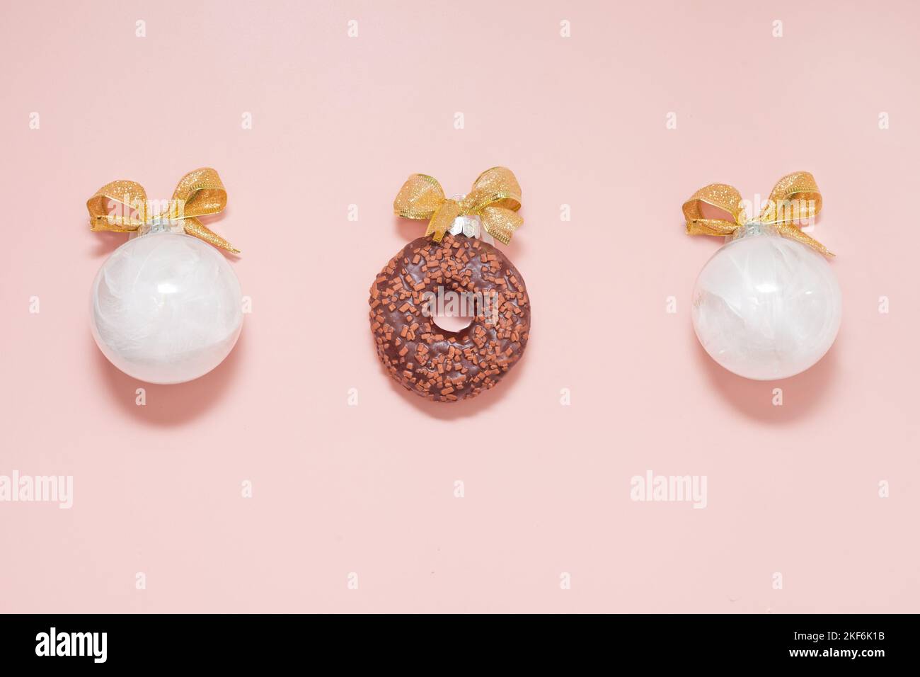 Weiße weihnachtskugeln mit Donut und goldenen Schleifen. Neujahr kreative Dekoration auf rosa Hintergrund Stockfoto