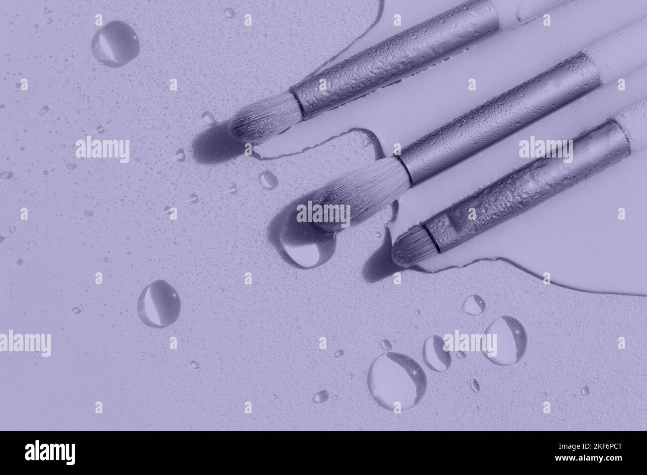 Digital Lavendel Farbe des Jahres 2023. Make-up Pinsel mit Wassertropfen auf einem hellvioletten Hintergrund. Foto ist von 2023 trendigen Farben getönt. Stockfoto