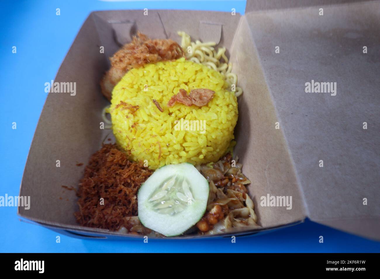 Indonesische traditionelle Gerichte, nämlich gelber Reis mit gebratener geriebener Kokosnuss, einfache Nudeln, Kartoffelkuchen, getrocknete Tempeh und eine Scheibe Gurke. Stockfoto