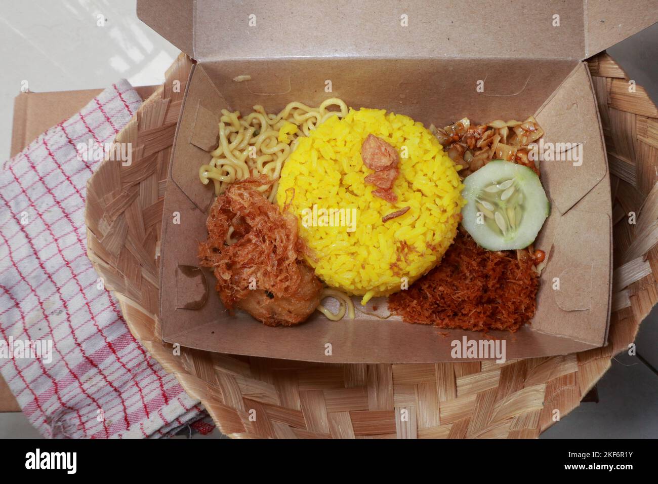 Ein Blick von oben auf traditionelle indonesische Speisen, nämlich gelber Reis mit gebratener geriebener Kokosnuss, einfache Nudeln, Kartoffelkuchen, getrocknete Tempeh und eine Scheibe Stockfoto