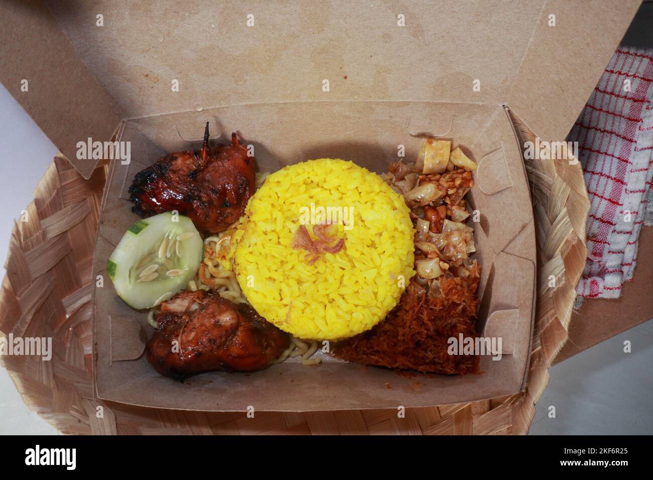 Draufsicht auf traditionelle indonesische Küche, nämlich Nasi Kuning mit zwei gegrillten Hühnern, gebratener Kokosraspel, einfachen Nudeln, getrocknetem Tempeh und einer Scheibe Stockfoto