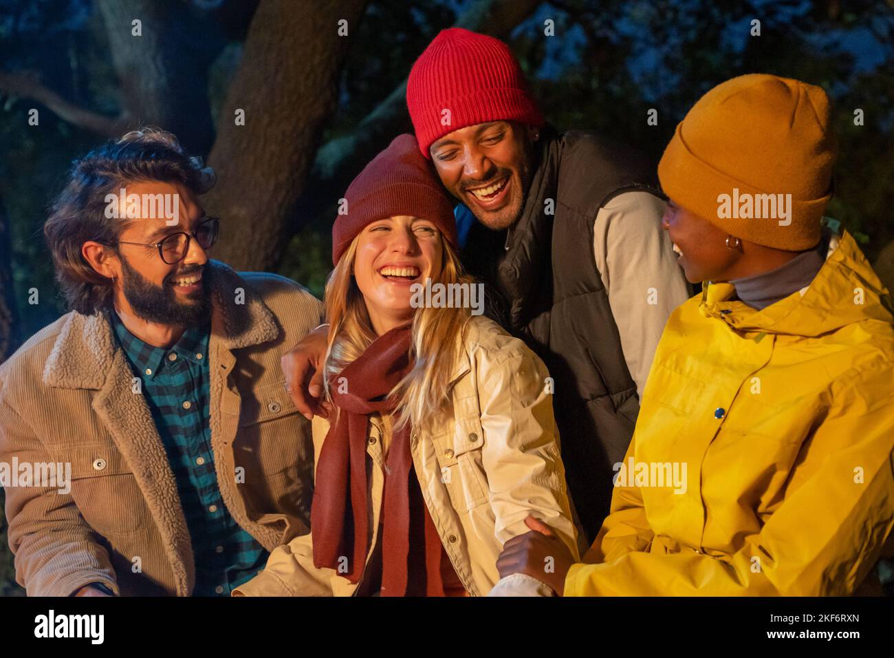Fröhliche, vielfältige Freunde haben Spaß beim Lachen neben dem Lagerfeuer in der Nacht kaukasische und schwarze Paare. Stockfoto