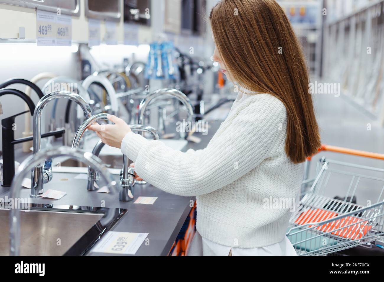 Hübsche junge Frau, die in einem Einrichtungsgeschäft eine Bad-/Küchenarmatur auswählt. Stockfoto