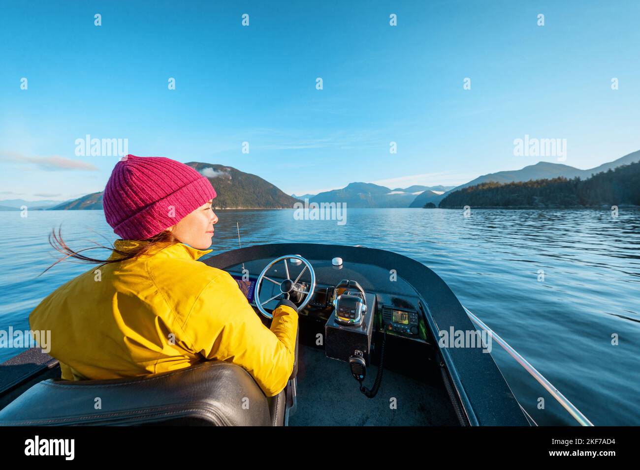 Frau fährt mit dem Motorboot in einer wunderschönen Naturlandschaft und lächelt glücklich beim Sonnenuntergang in der Küstenregion British Columbia in der Nähe von Bute, Toba Inlet und Campbell River Stockfoto