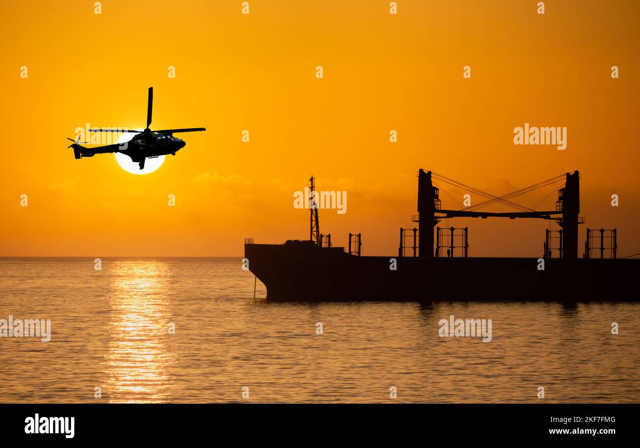 Militärhubschrauber, der bei Sonnenuntergang über einem Öltanker fliegt Stockfoto