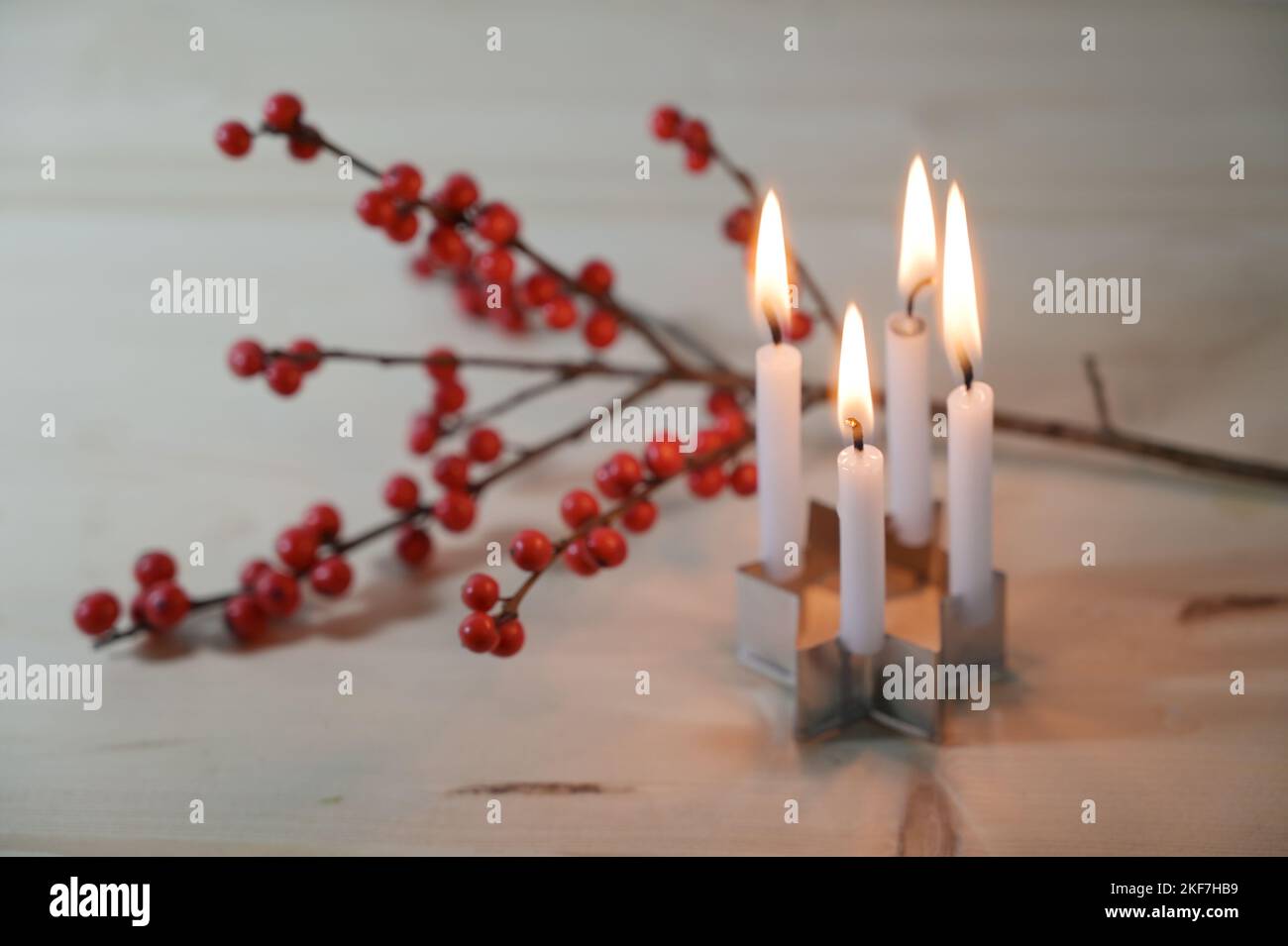 Mini-Adventskranz, vier kleine Kerzen auf einem Keksschneider in Sternform vor einem Stechenzweig mit roten Beeren auf einem Holztisch, ausgewählter Fokus, Stockfoto