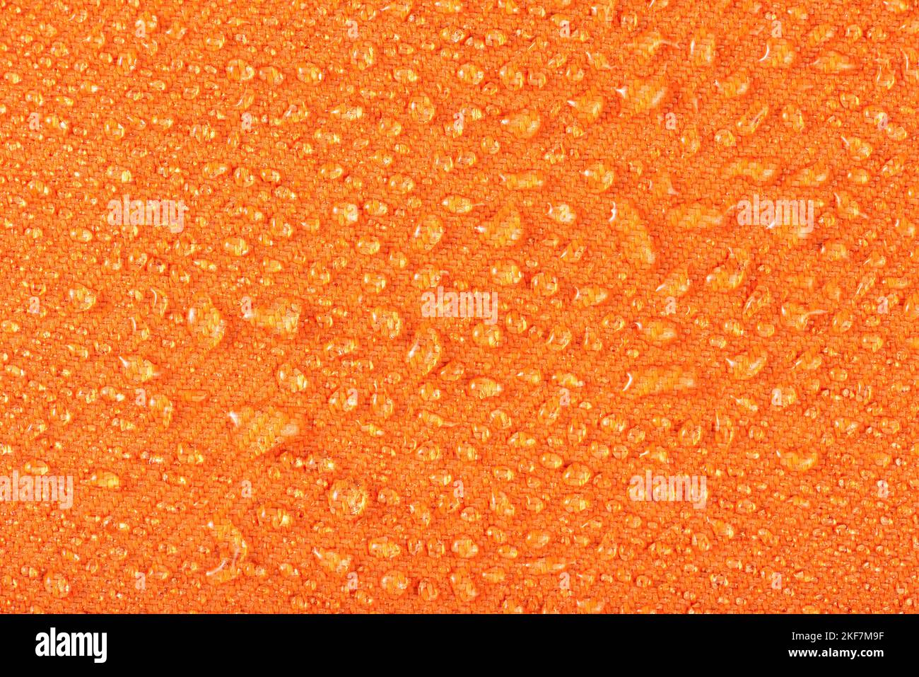 Wasserdichte Kleidung oder Polstermöbel aus wasserdichten Textilien. Wassertropfen auf orangefarbene Textilien mit wasserabweisenden Eigenschaften. Stockfoto