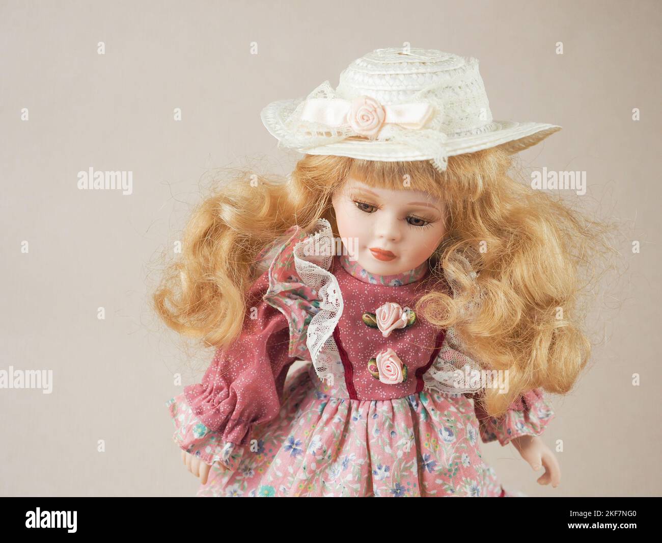 Vintage Porzellan Puppe goldhaarig Mädchen mit fließenden Haaren mit braunen Augen in einem rosa Kleid und einem Strohhut Stockfoto